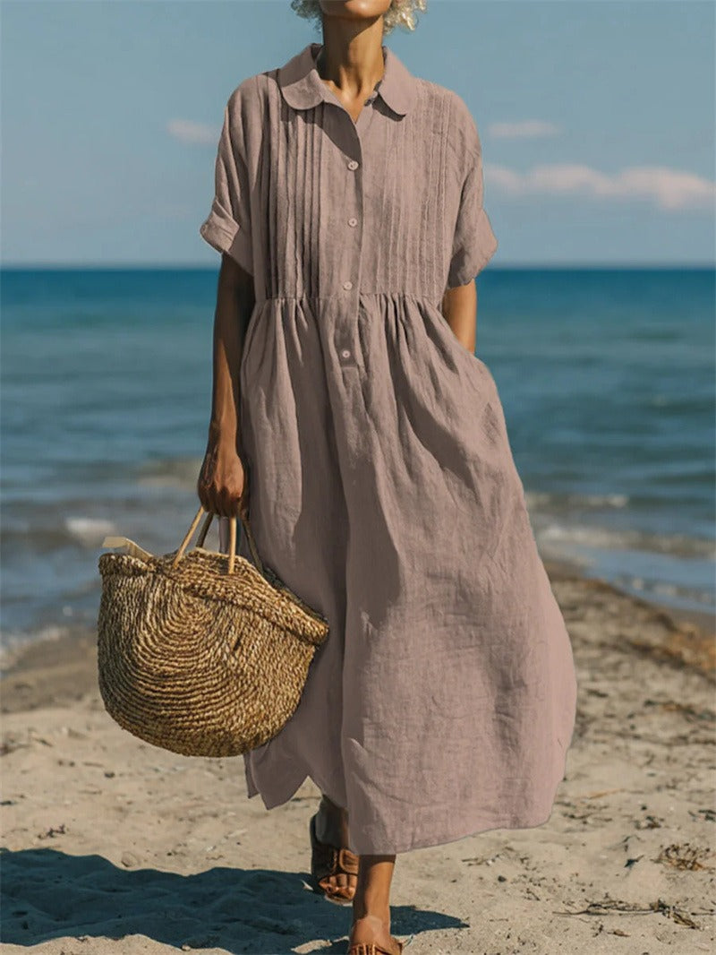Taupe linen-look maxi shirt dress with pintuck bodice, button placket, and short sleeves worn on a beach.
