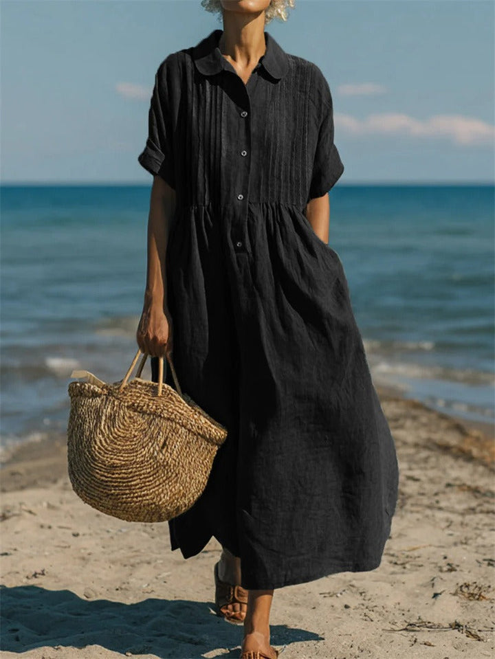 Black linen-look maxi shirt dress with pintuck bodice, button placket, and short sleeves worn on a beach.
