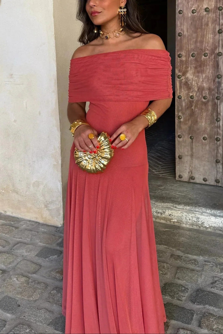 Woman wearing a coral-colored, off-the-shoulder pleated maxi dress with a fluid, lightweight silhouette.