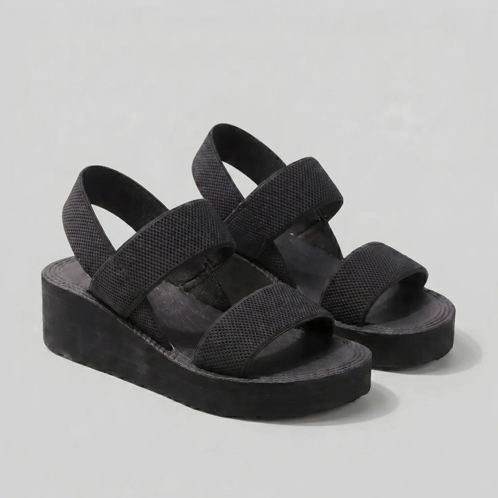 Black sandals with multiple straps on a light gray background