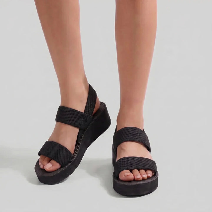 Black sandals worn on feet against a light gray background