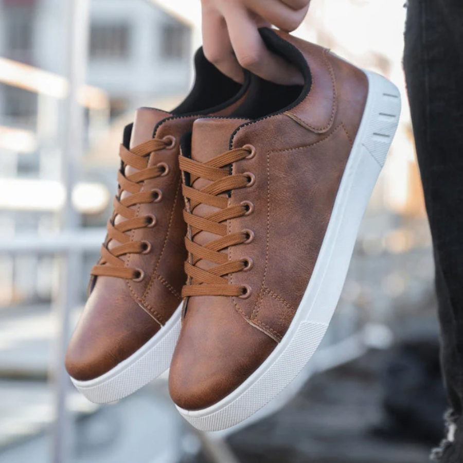 Brown faux leather lace-up sneakers with a minimalist design and a crisp white rubber sole held by a hand.