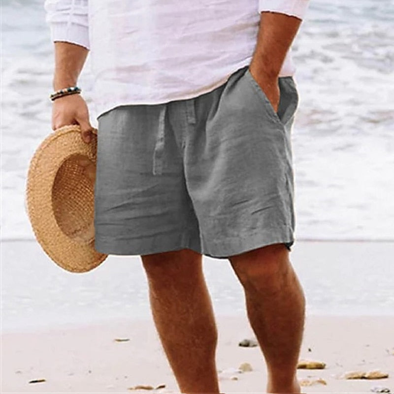 Men's grey linen beach shorts featuring a relaxed fit, elasticated drawstring waist, and side pockets on a sandy beach.