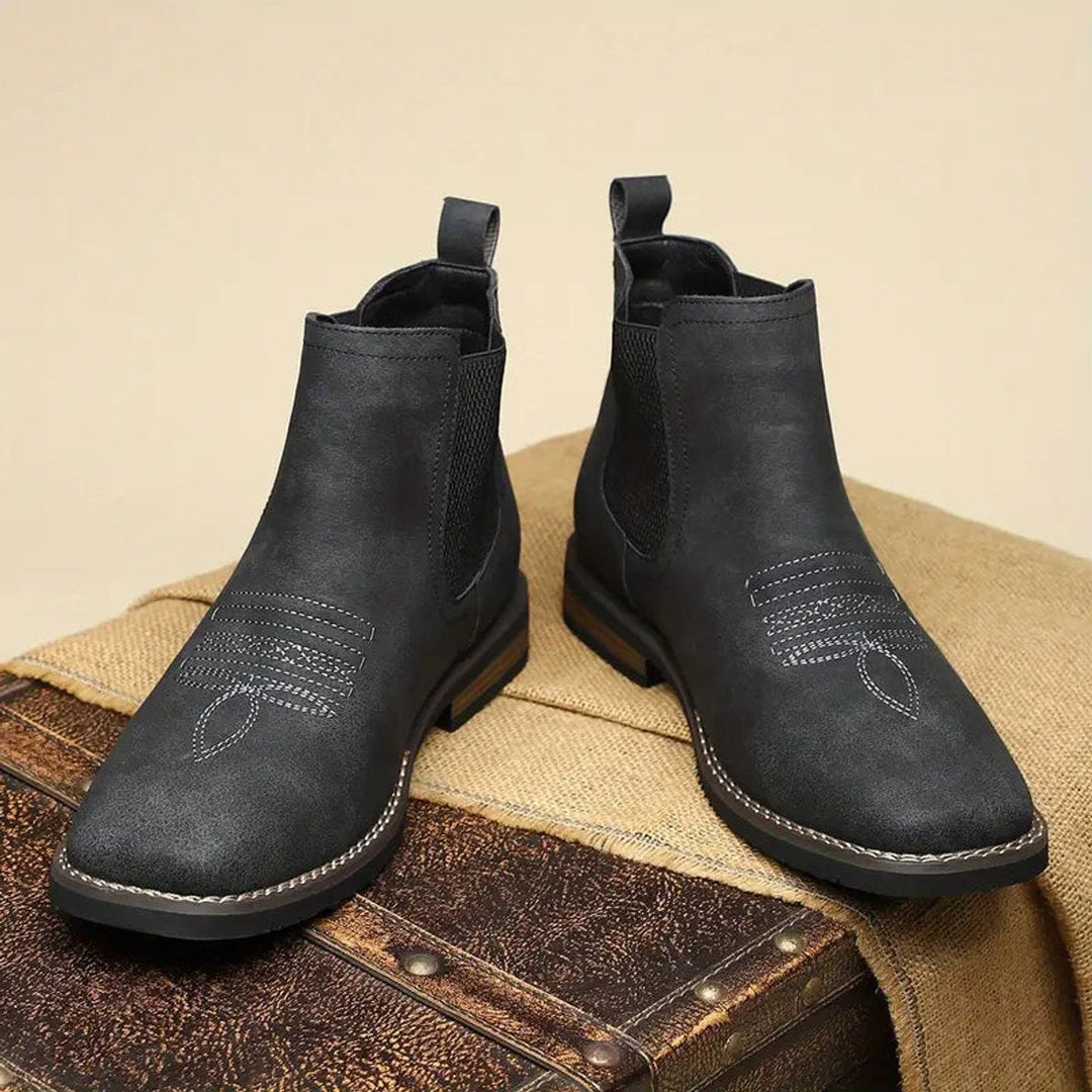 Black distressed faux leather Western Chelsea boots with elastic side panels, pull tabs, and decorative toe stitching.