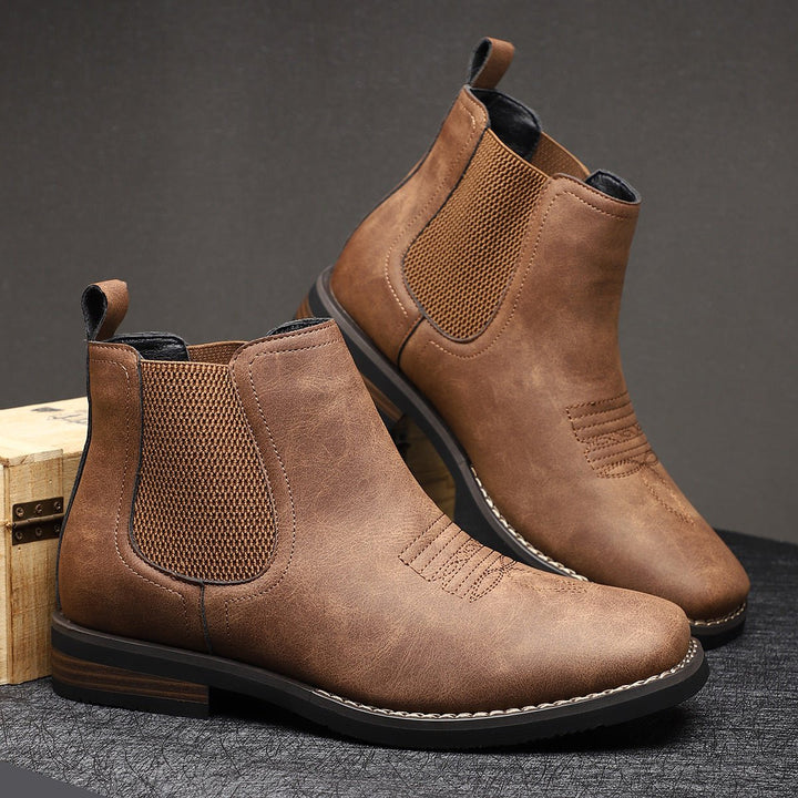Brown distressed faux leather Chelsea boots with western-style toe stitching, elastic side panels, and stacked block heels.