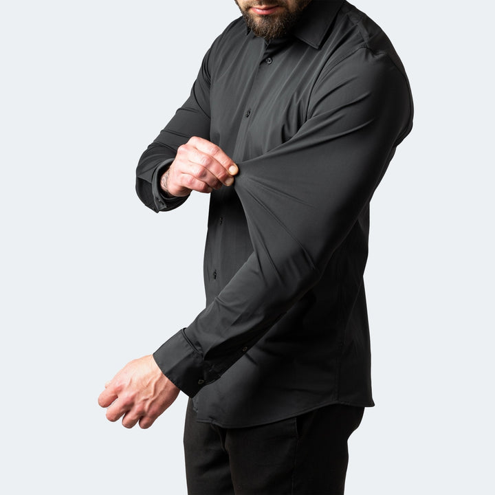 Man wearing a black slim-fit stretch dress shirt, demonstrating the flexible, high-stretch fabric on the sleeve.