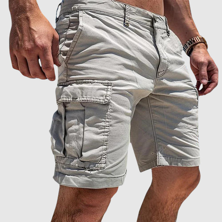 Beige knee-length cargo shorts in soft washed cotton with side flap pockets and a relaxed athletic fit.