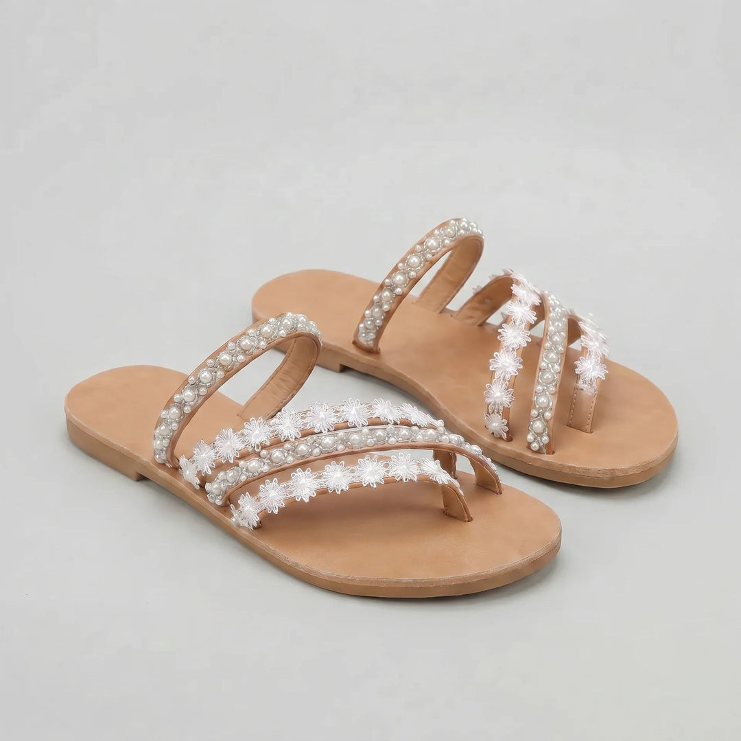 Pair of beige sandals with pearl embellishments on a light gray background