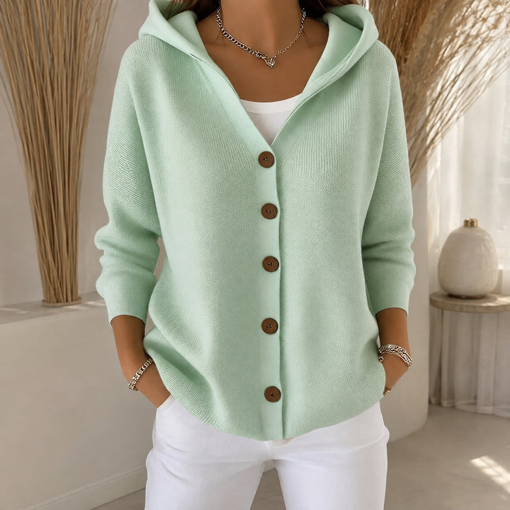 Soft mint green knitted cardigan featuring a cozy hood and wooden-effect buttons for a relaxed, layered look.