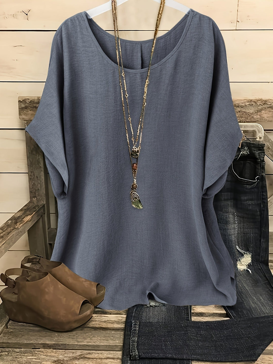 Blue linen-look round neck top with batwing sleeves, styled with a layered necklace, distressed jeans, and wedges.