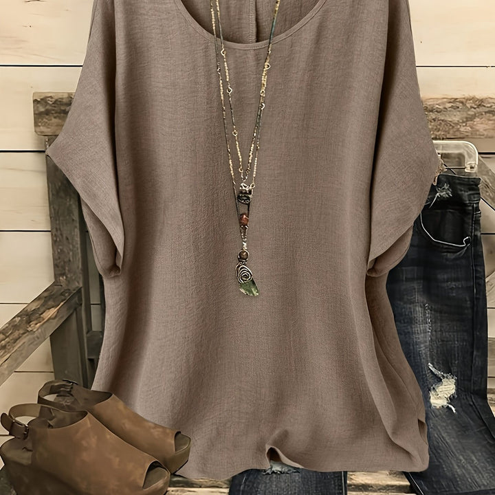 Taupe linen-look round neck top with batwing sleeves, styled with a layered necklace and distressed jeans.