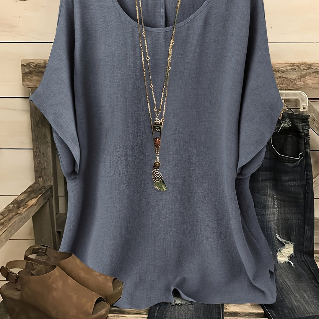 Blue linen-look round neck top with batwing sleeves, styled with a layered pendant necklace and jeans.
