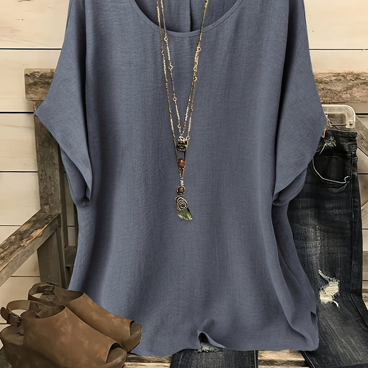 Blue linen-look round neck top with batwing sleeves, styled with a layered pendant necklace and jeans.