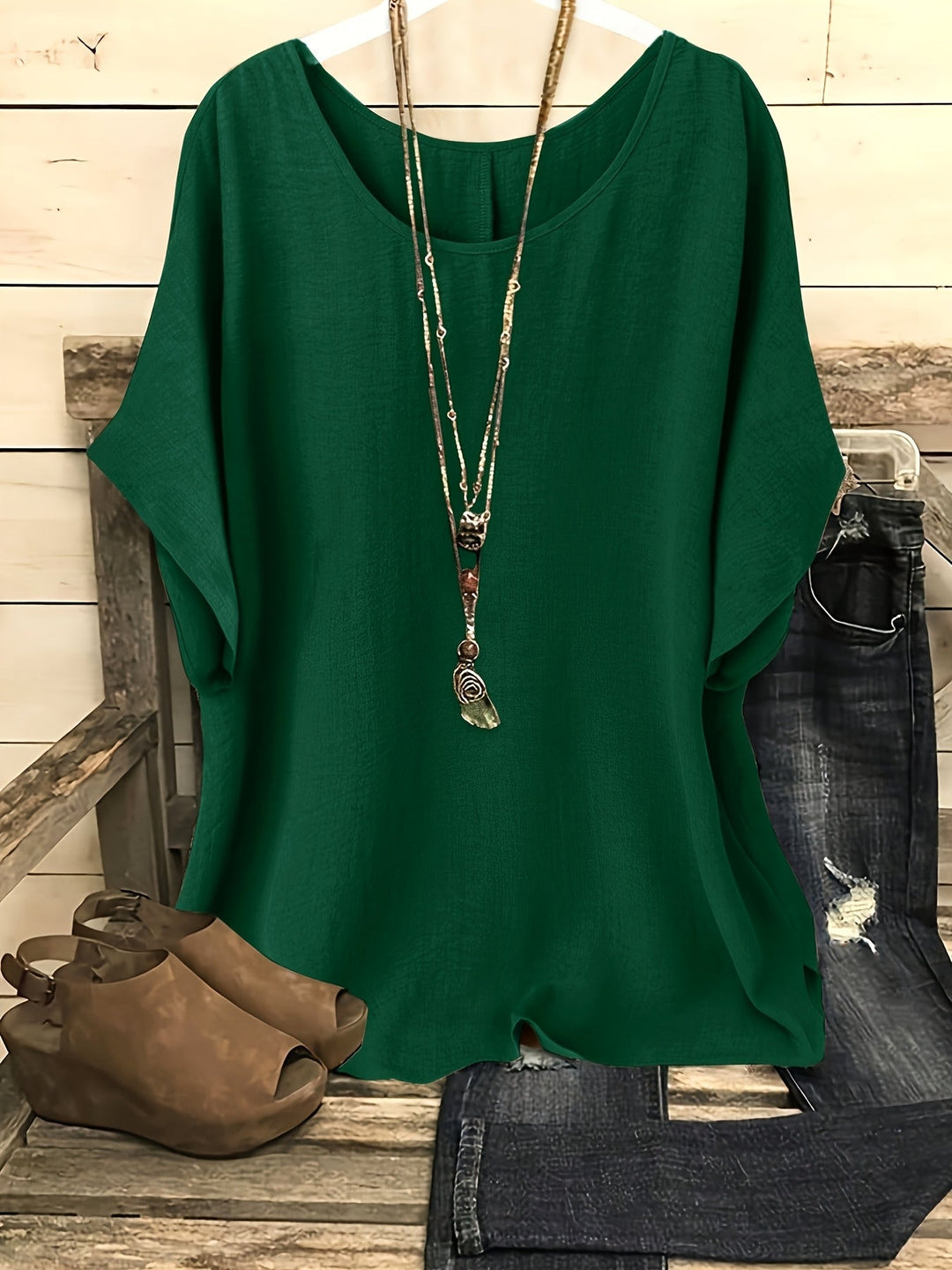 Dark green linen-look top with a round neck and relaxed batwing sleeves, styled with a layered necklace.