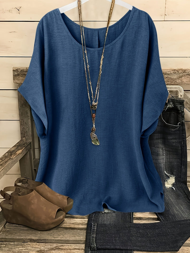 Blue linen-look round neck top with batwing sleeves, styled with a layered necklace, dark jeans, and brown sandals.