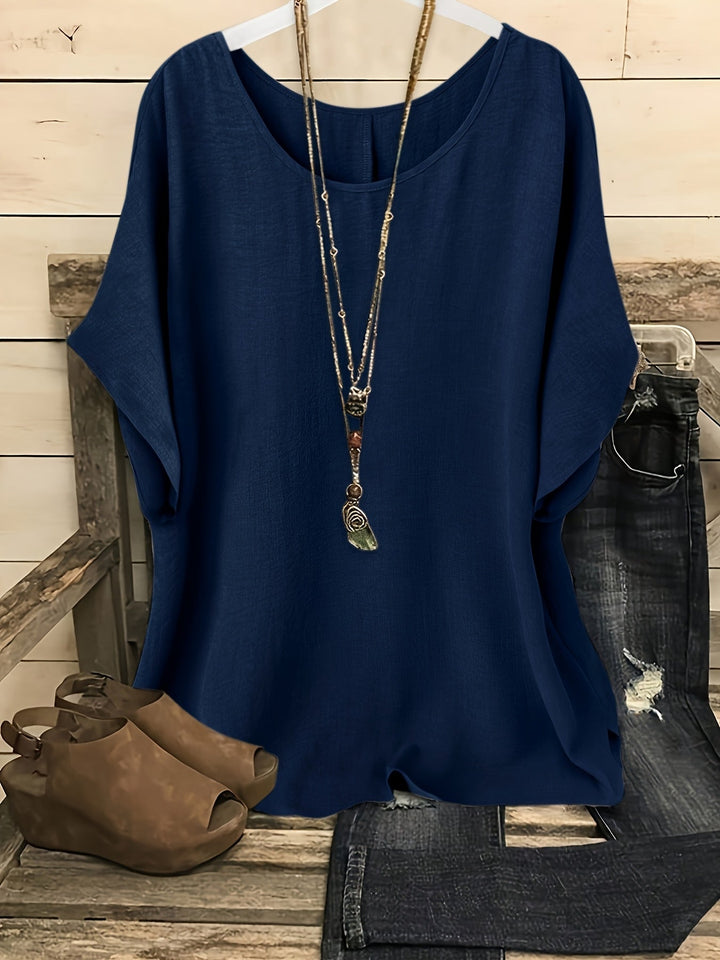 Navy blue linen-look round neck top with batwing sleeves, styled with a layered necklace, jeans, and wedge sandals.