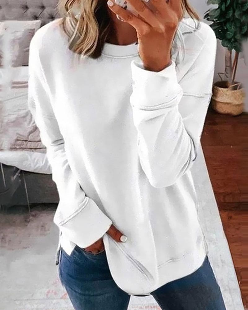 White long-sleeve crew neck sweatshirt with a relaxed fit, ribbed cuffs, and side hem slits worn with blue jeans.