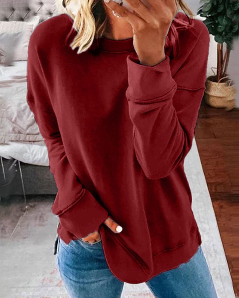 Burgundy crew neck long sleeve sweatshirt with a relaxed fit, ribbed cuffs, and side hem slits worn with blue jeans.