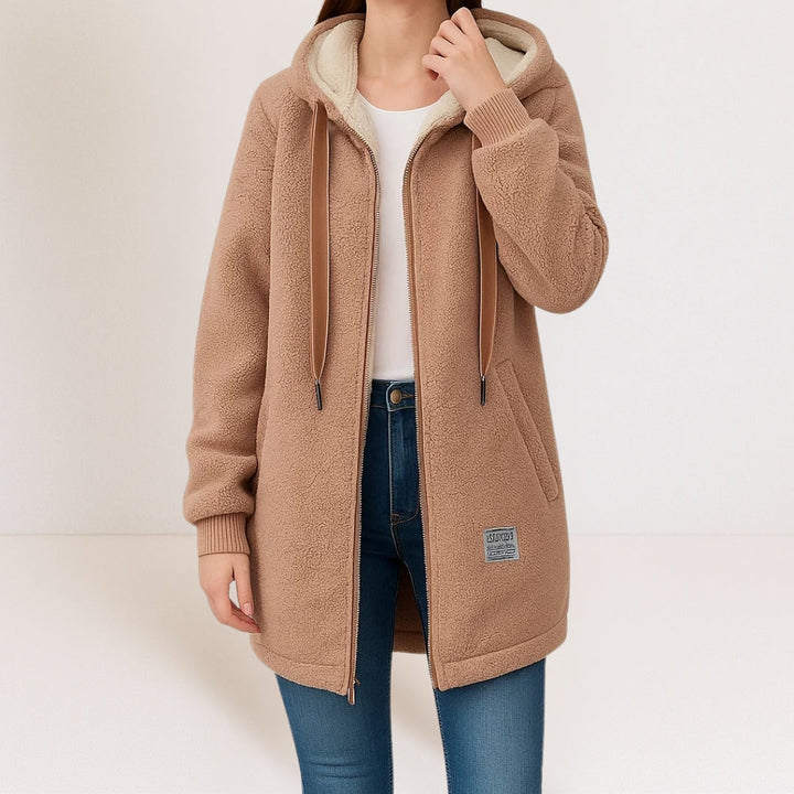 Tan longline sherpa fleece jacket with a cream-lined hood, full-length zip, and ribbed cuffs worn over blue jeans.