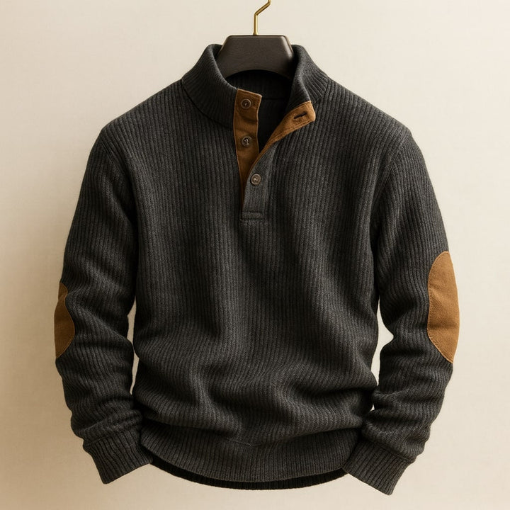 Charcoal grey ribbed knit jumper with a button-neck placket and brown suede elbow patches on a hanger.
