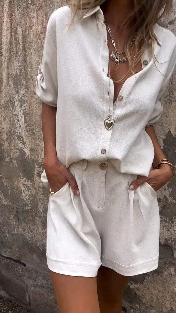 Woman wearing a white linen button-up shirt with rolled sleeves and matching pleated shorts with side pockets.