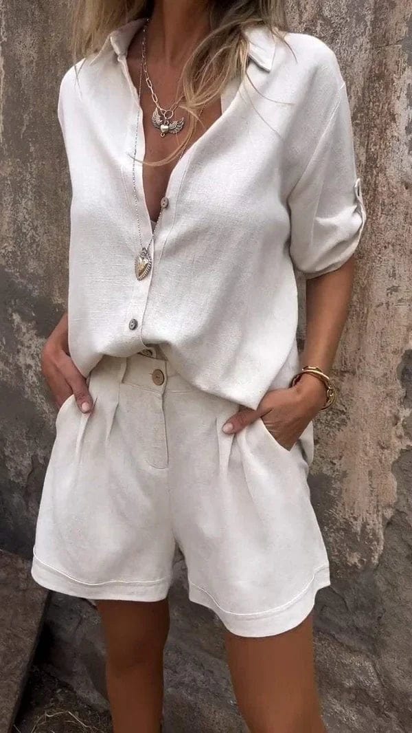 Woman wearing a beige linen two-piece set featuring a collared button-up shirt with roll-up sleeves and pleated shorts with pockets.