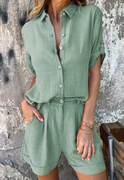 Sage green linen two-piece set featuring a collared button-up shirt with roll-up sleeves and matching pleated shorts.