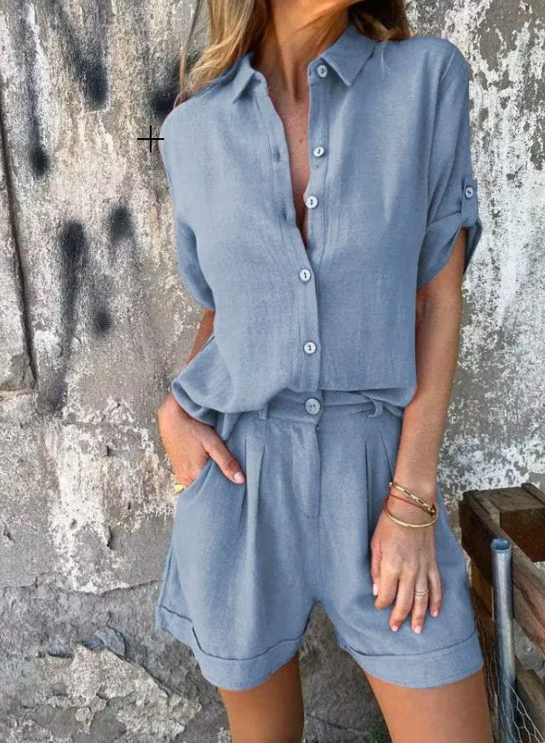 Blue linen two-piece set featuring a collared button-up shirt with roll-up sleeves and matching pleated shorts with pockets.