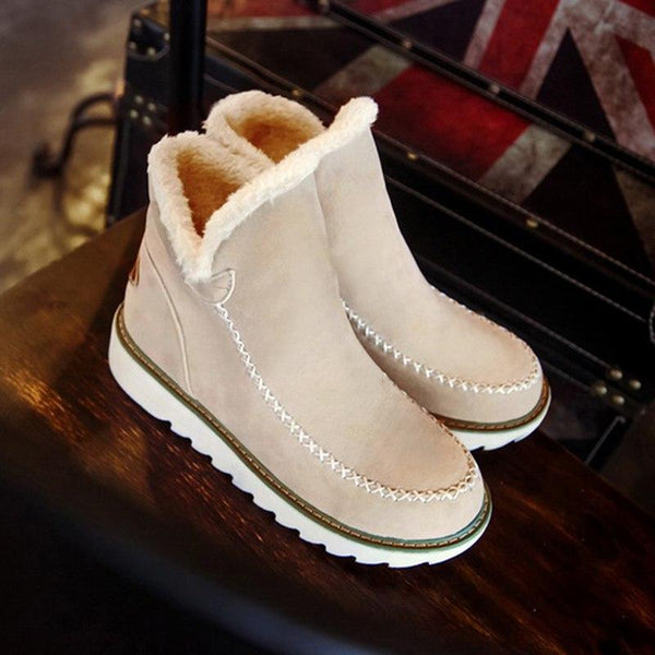 Beige suede-look ankle boots with plush faux fur trim, moccasin stitching, and a grippy white ribbed sole for winter.