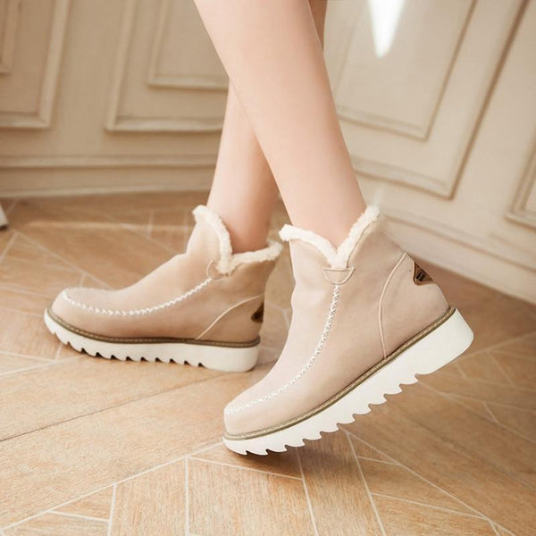 Beige suede-look ankle boots with plush faux fur trim, moccasin-style stitching, and a white grippy ribbed sole.