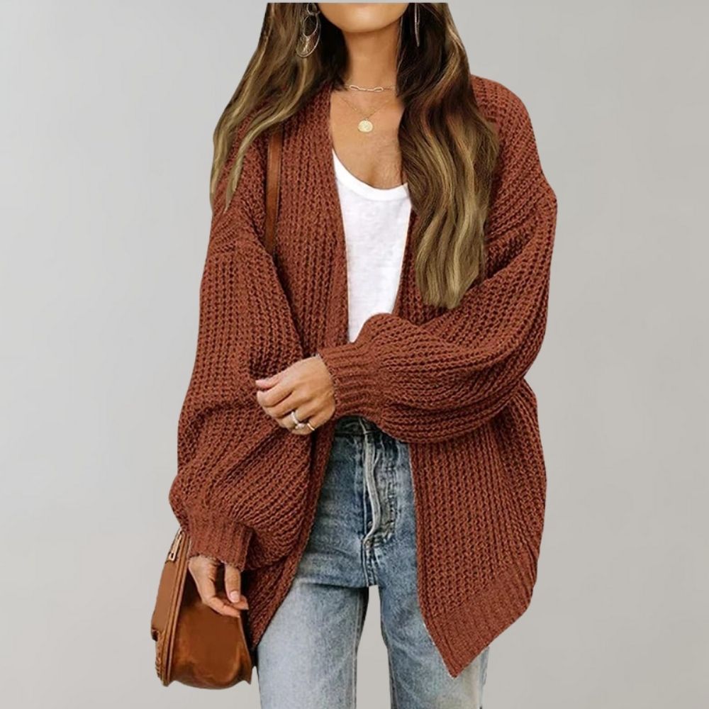 Rust-colored chunky knit oversized cardigan with an open front and balloon sleeves worn over a white top and jeans.