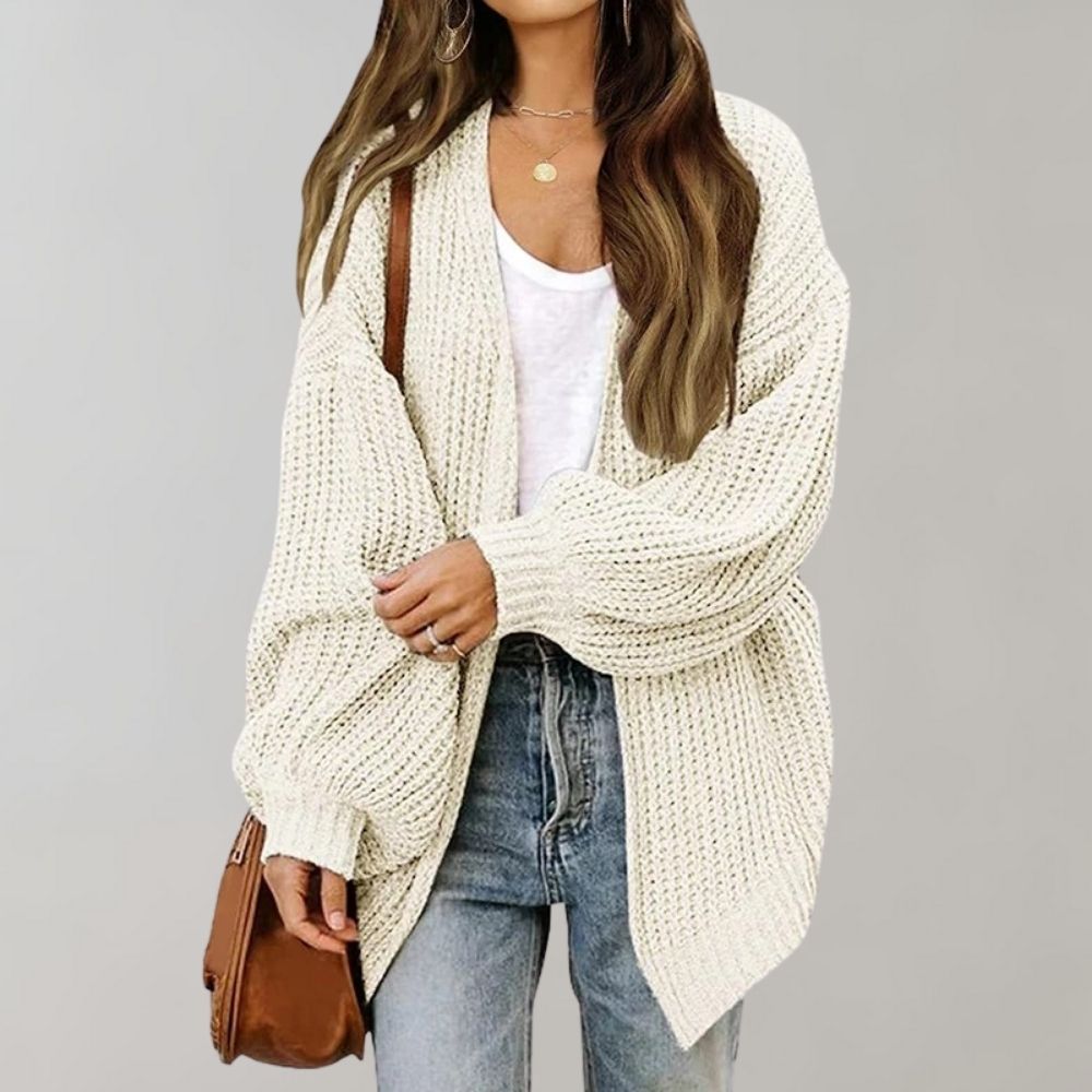 Cream chunky knit oversized cardigan with an open front and balloon sleeves worn over a white tee and blue jeans.