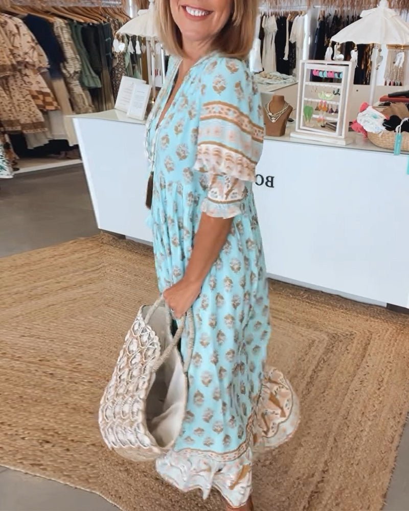 Matilda floral V-neck maxi dress in light blue with brown and white print, worn by a woman carrying a woven bag.