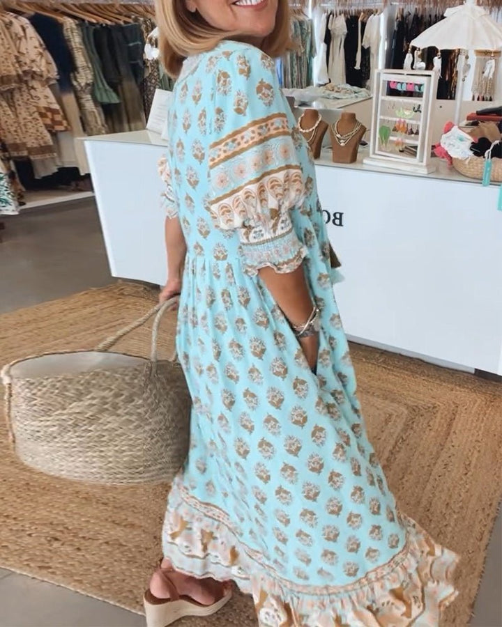 Matilda floral V-neck maxi dress in light blue with brown print, flowing fabric, and ruffled hem.