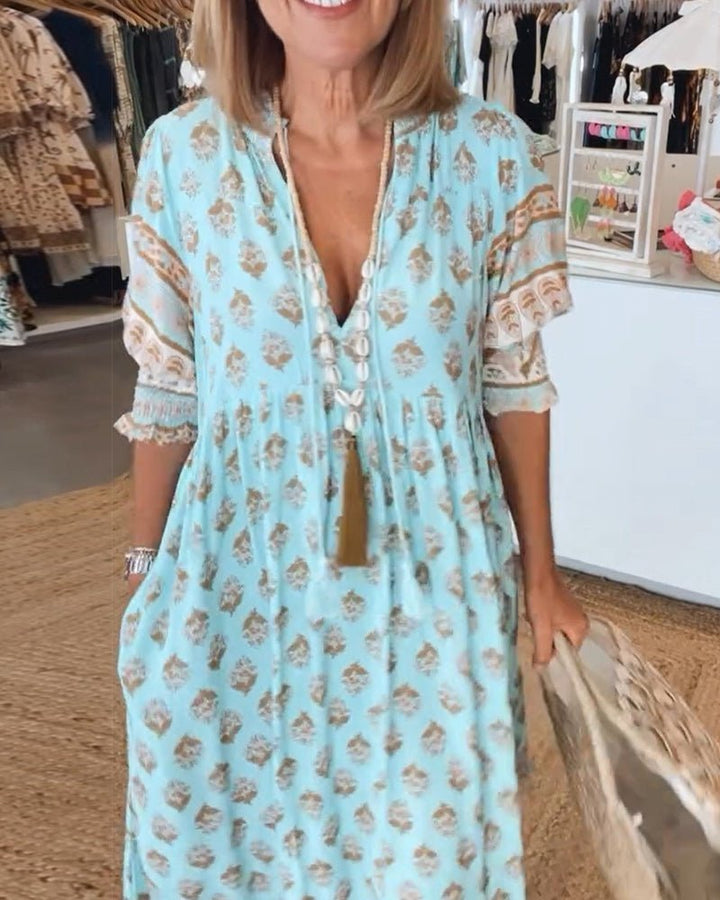Matilda Women's Floral V-Neck Maxi Dress in light blue with brown print, flowing fabric, and tassel necklace.