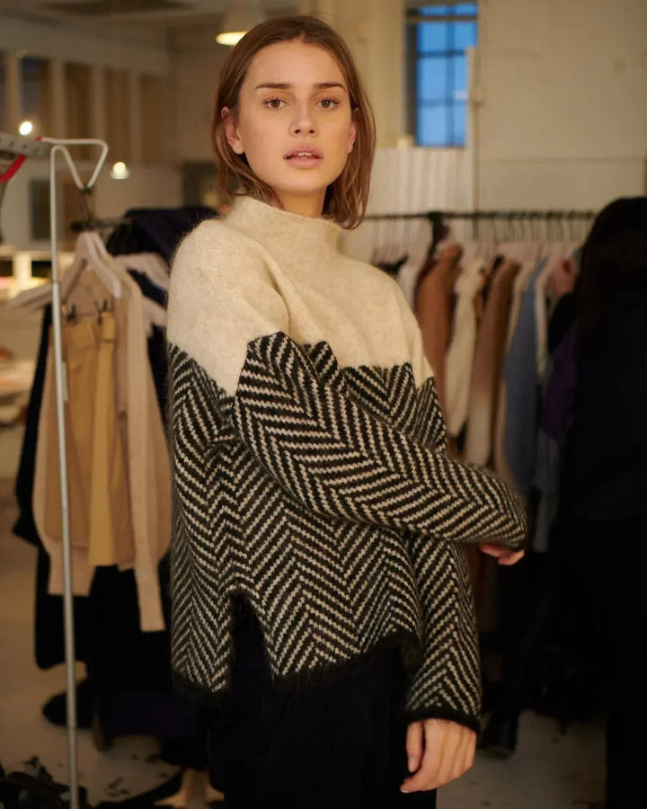 Woman wearing a cosy, oversized high-neck jumper with a two-tone cream and black herringbone knit pattern.
