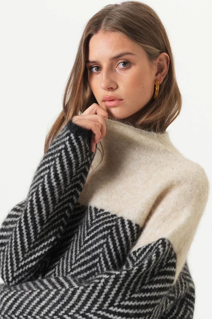 Woman wearing a cosy, oversized high-neck jumper with a black and cream two-tone herringbone knit pattern.