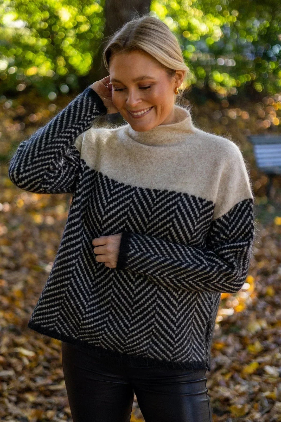 Woman wearing an oversized, high-neck jumper with a black and cream two-tone herringbone knit pattern outdoors.