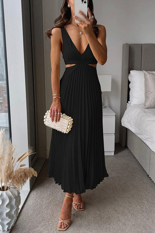Woman wearing a black satin midi dress with a V-neck, waist cut-outs, and a pleated skirt, styled with strappy heels.