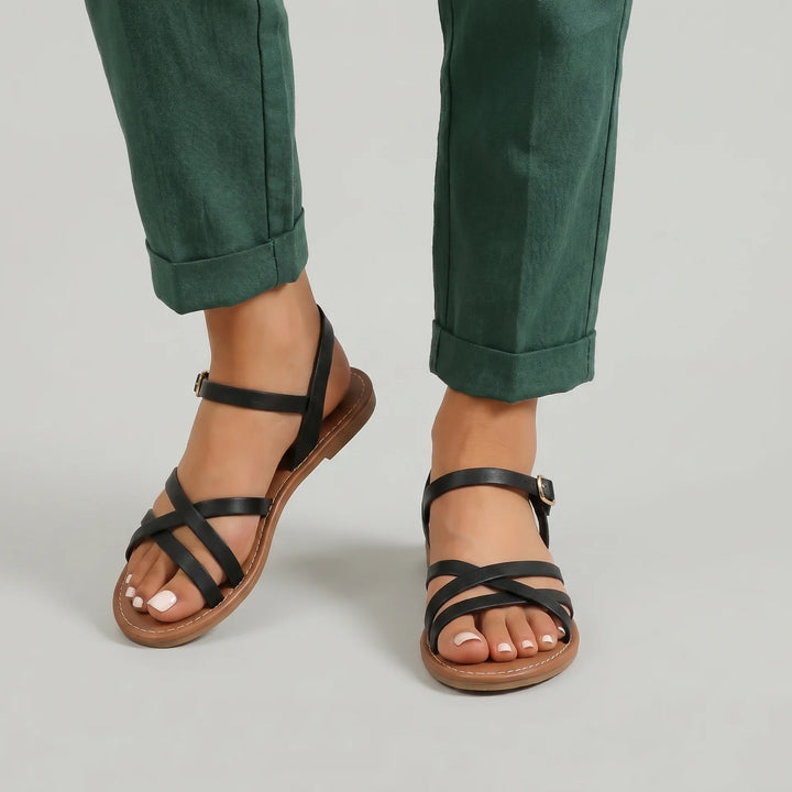 Black strappy sandals worn with green pants on a neutral background