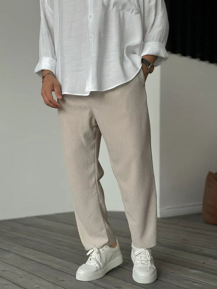 Beige men's tapered trousers featuring a vertical ribbed texture and elasticated waist, styled with a white shirt and sneakers.