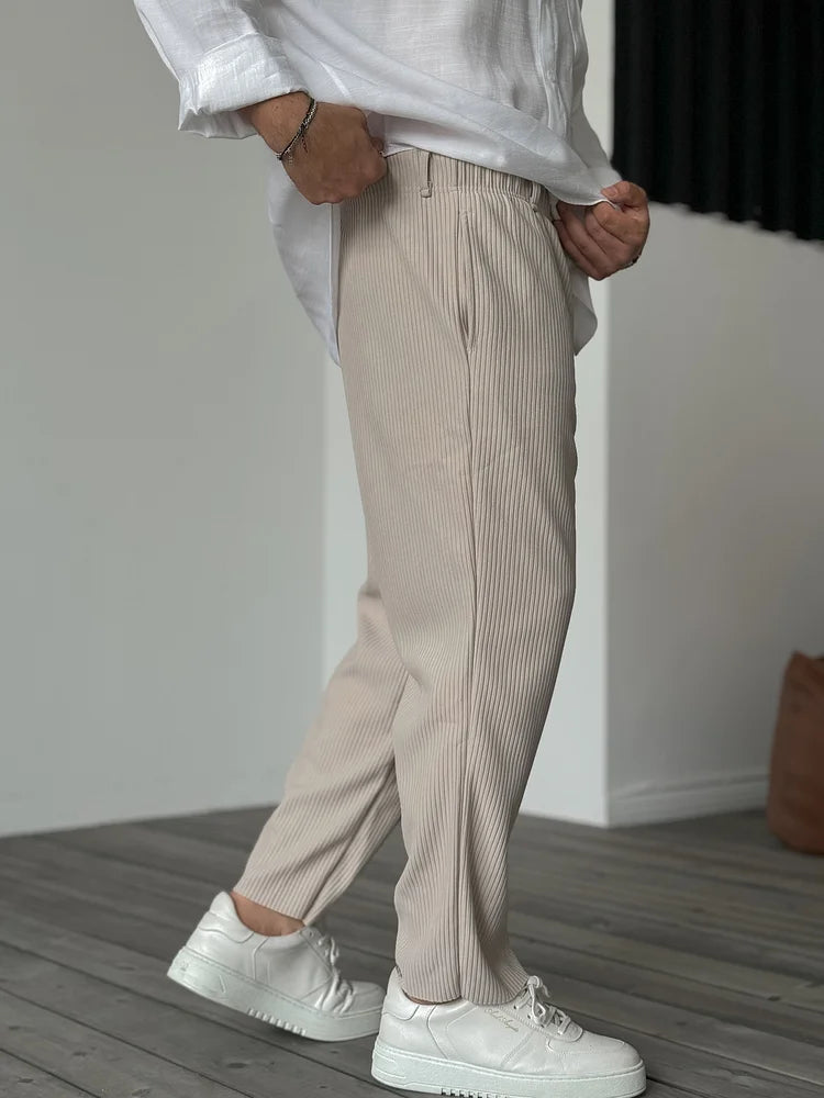 Beige men's tapered trousers with a vertical ribbed texture, elasticated waist, and relaxed fit worn with white sneakers.