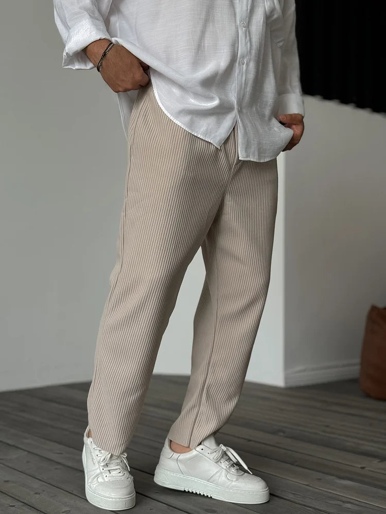 Beige tapered trousers with a vertical ribbed texture and elasticated waist, styled with a white shirt and sneakers.