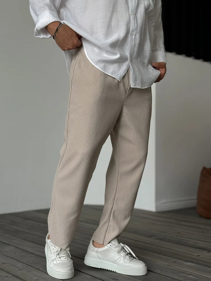 Beige tapered trousers with a vertical ribbed texture and elasticated waist, styled with a white shirt and sneakers.