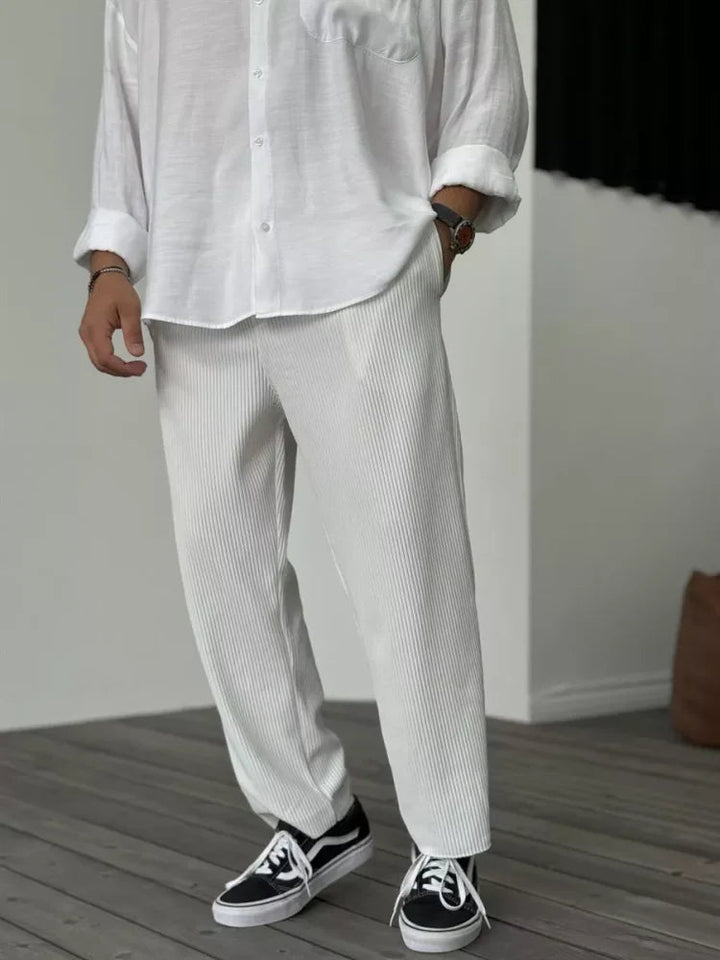 Off-white tapered trousers with a vertical ribbed texture and elasticated waist, styled with a white shirt.