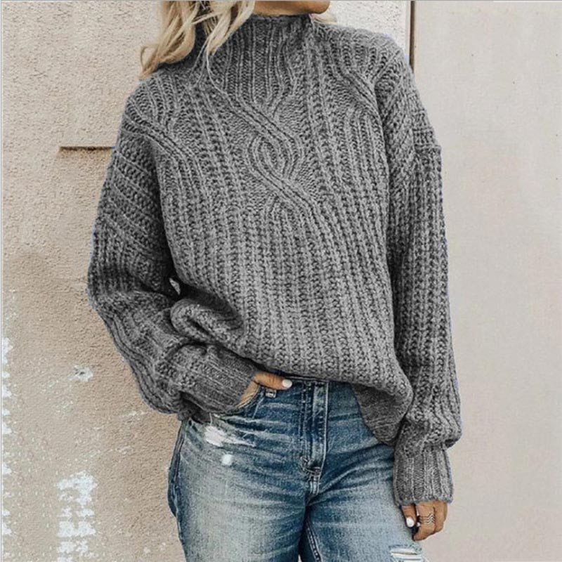 Grey cable-knit mock neck jumper with a relaxed, chunky texture and long sleeves worn with blue jeans.