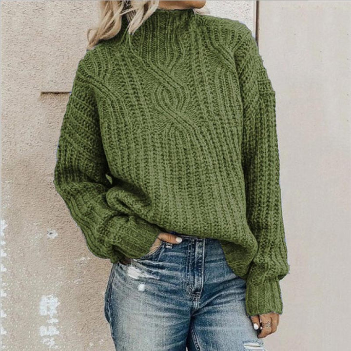 Olive green chunky cable-knit jumper with a mock neck and relaxed fit worn with blue jeans.