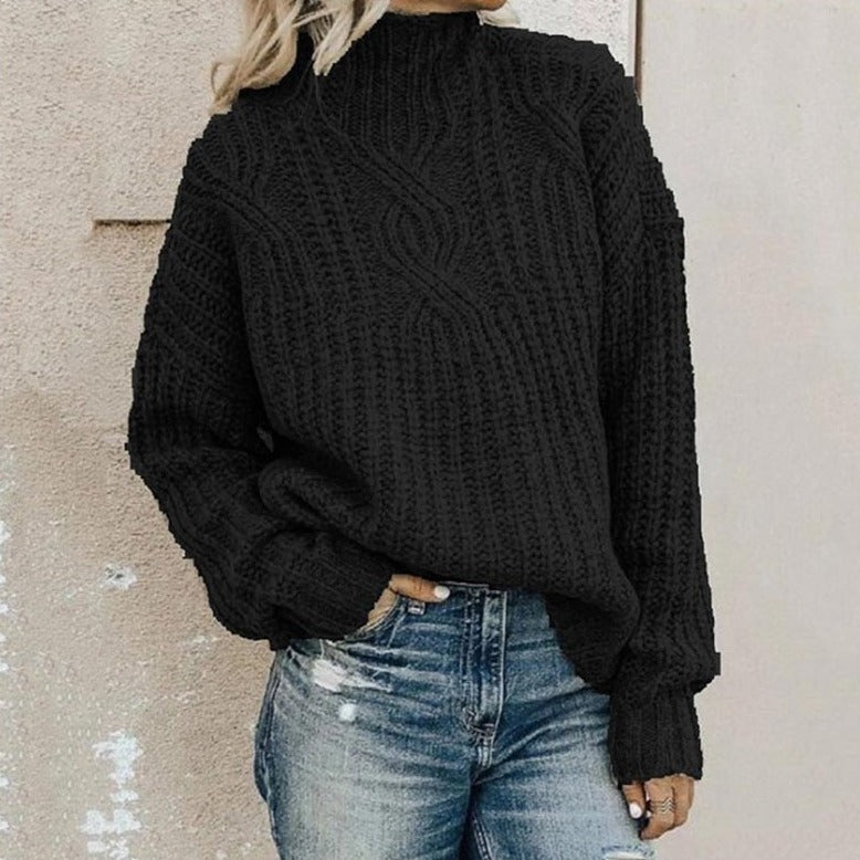 Black cable-knit jumper with a mock neck and relaxed fit, styled with blue distressed jeans.