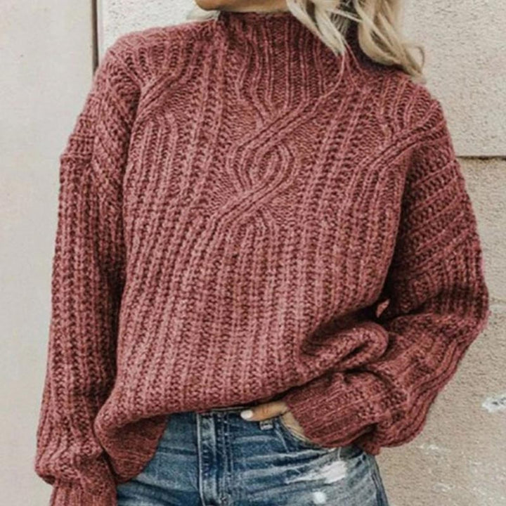 Dusty rose cable-knit jumper with a mock neck and relaxed fit, styled with blue denim jeans.