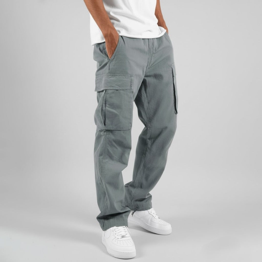 Men wearing grey relaxed-fit cotton cargo trousers with side pockets and white sneakers against a grey background.